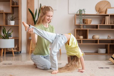 Küçük kızıyla birlikte oturma odasında yoga yapan genç ve güzel bir kadın.