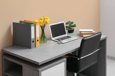 Kitapları, narsisli çiçekleri ve bej duvarın yanındaki açık ofis bilgisayarlı şık bir iş yeri.