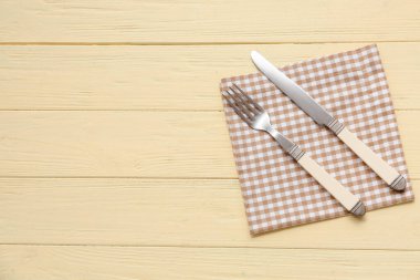 Sarı ahşap arka planda peçete, çatal ve bıçaklı masa.