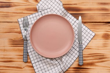 Tabak, çatal bıçak takımı ve tahta arka planda kareli peçete.