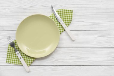 Tabak, çatal bıçak takımı ve bej ahşap arka planda kareli peçete.