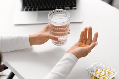 Beautiful young woman with healthy fish oil capsules and glass of water at home, closeup