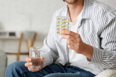 Su toplamış balık yağı kapsülleri ve su taşıyan yakışıklı genç adam evdeki kanepede oturuyor, yakın plan.