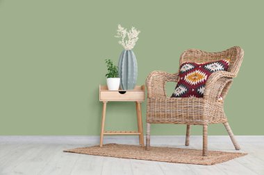 Masadaki yapay bitkiler ve oturma odasındaki yeşil duvarın yanındaki hasır koltuk.