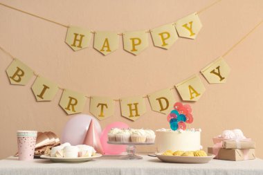 Bej duvara karşı doğum günü partisi için farklı tatlılar ve dekorlarla dolu bir masa.