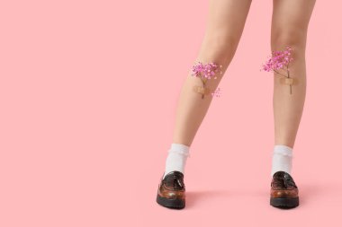 Pembe arka planda çingene çiçekleri olan deri ayakkabılı kadın bacaklar.