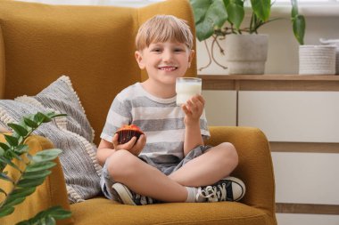 Evdeki koltukta oturan bir bardak sütü ve keki olan sevimli küçük çocuk.