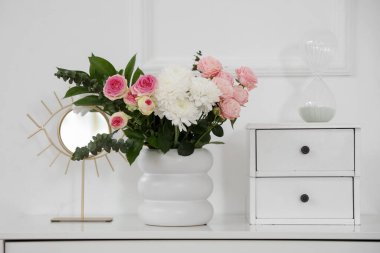 Çiçekli vazo ve çekmecelerin üstündeki ayna şık oturma odasında, yakın plan.