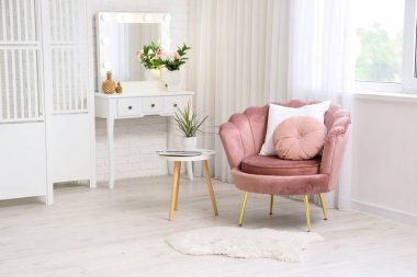 İçinde pembe koltuk, çekmece, vazo, çiçek ve sehpa olan oturma odası.