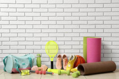 Beyaz tuğla duvarın yanında farklı spor aletleri, çanta ve spor ayakkabıları.