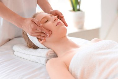 Spa salonunda yaşlanmayı önleyen yüz masajı yaptıran genç bir kadın.