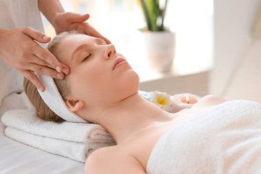 Spa salonunda yaşlanmayı önleyen yüz masajı yaptıran genç bir kadın.