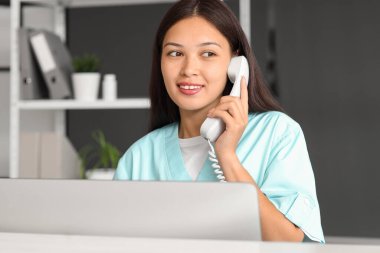Hastanede telefonla konuşan genç bir kadın resepsiyonist.