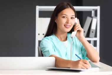 Hastanedeki not defterine telefonla konuşan genç bir tıbbi resepsiyonist.