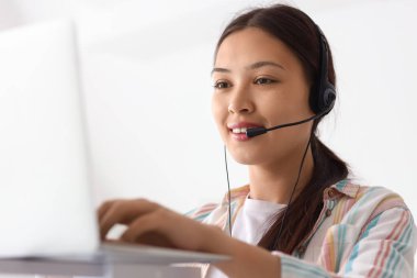 Kulaklıklı genç bayan resepsiyonist ofiste modern dizüstü bilgisayarla çalışıyor.