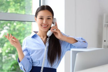 Genç bayan resepsiyonist ofiste telefonla konuşuyor.