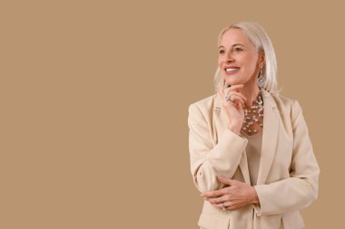 Kahverengi arka planda güzel mücevherleri olan modaya uygun olgun bir kadın.