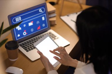 Tablet bilgisayarı ve dizüstü bilgisayarı olan bir kadın karanlık ofiste masa başında çalışıyor. İkinci kavram