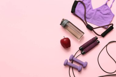 Elma, spor giyim ve pembe arka planda farklı spor ekipmanları.