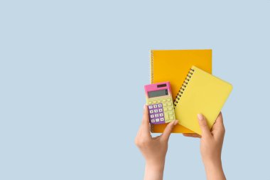 Mavi arkaplanda not defterleri ve hesap makinesi olan kadın elleri