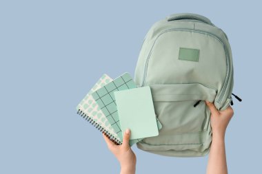 Mavi arka planda not defterleri ve sırt çantalı kadın elleri