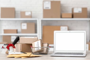 Paket kutularıyla dolu boş bir dizüstü bilgisayar ve posta deposundaki masada bant dağıtıcısı.