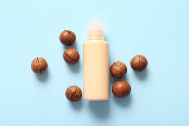 Mavi arka planda Macadamia fındıkları ve bir şişe kozmetik ürünü.