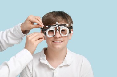 Mavi arka plandaki küçük çocuk için optik deneme çerçevesini özelleştiren kadın göz doktoru.