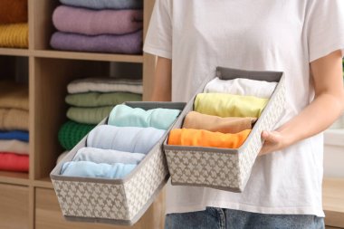 Evde katlanmış temiz giysileri olan organizatörleri tutan genç bir kadın var.