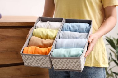 Evde katlanmış temiz giysileri olan organizatörleri tutan genç bir kadın var.