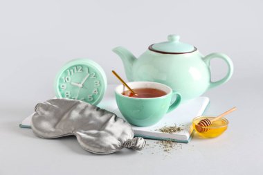 Uyku maskesi, alarm saati ve gri arkaplanda çay seti