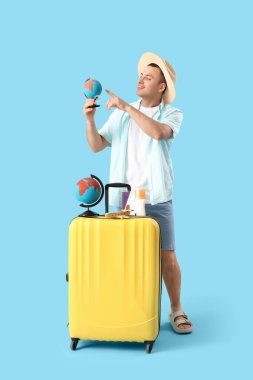 Mavi arka planda bavulu ve küresi olan erkek turist.