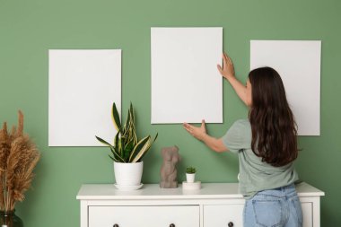 Evdeki yeşil duvara boş tuval asan genç bir kadın. Arka plan
