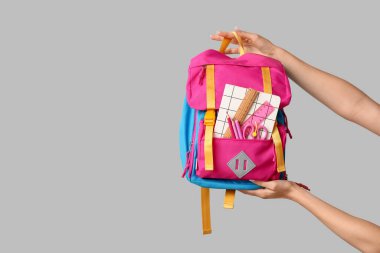 Sırt çantalı kadın eller ve gri arka planda farklı okul malzemeleri, yakın plan.