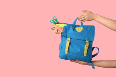 Sırt çantalı kadın eller ve pembe arka planda farklı okul malzemeleri, yakın plan.