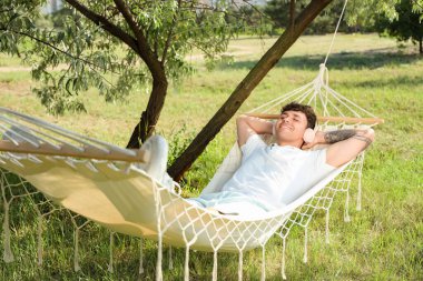 Kulaklıklı genç adam dışarıda hamakta dinleniyor.