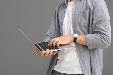 Gri arkaplanda modern laptop kullanan erkek programcı, yakın plan