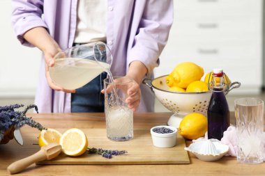 Mutfaktaki masada lavanta limonatası hazırlamak için limon suyunu bardağa dolduran genç bir kadın.