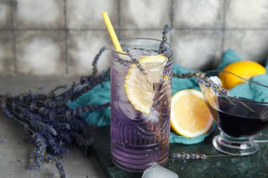 Lezzetli bir bardak lavantalı limonata, şurup ve masadaki çiçekler grunge fayans duvarına karşı.