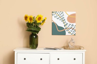 İçinde güzel ayçiçekleri olan vazolar, heykelcikler ve oturma odasındaki çekmecelerin üstündeki dergiler.