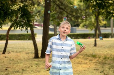 Parkta sabun köpüğü üfleyen şirin, mutlu küçük çocuk.