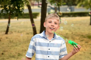 Parkta sabun köpüğü üfleyen şirin, mutlu küçük çocuk.