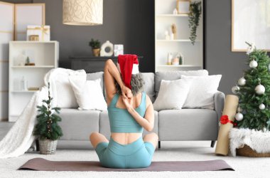 Noel Baba şapkalı sportif kadın Noel arifesinde evde yoga yapıyor.