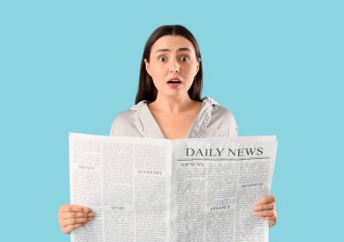 Mavi arka planda gazete okuyan pijamalı genç kadın şok oldu.