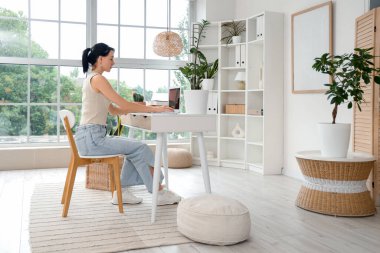 Ev ofisteki masada dizüstü bilgisayarla çalışan genç bir kadın.