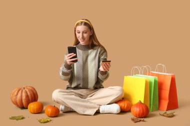 Cep telefonu ve kredi kartı alışverişi yapan genç bir kadın kahverengi arka planda