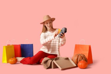 Sonbahar kıyafetleri içinde ödeme terminali ve pembe arka planda kredi kartı olan genç bir kadın. İnternetten alışveriş