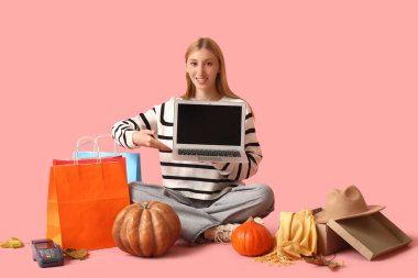 Boş dizüstü bilgisayarı ve pembe arka planda alışveriş torbaları olan genç bir kadın.