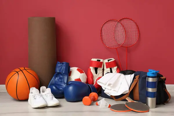 stock image Different sports equipment and white sneakers on floor near red wall