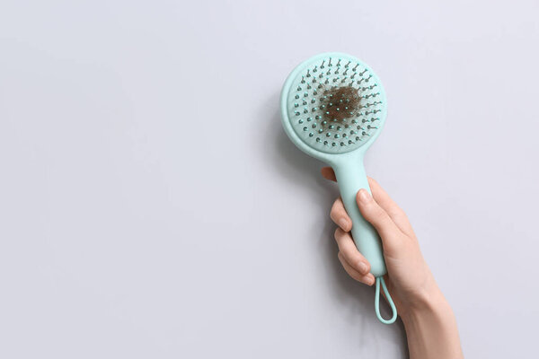 Рука с расчёской и куском волос на сером фоне. Концепция выпадения волос